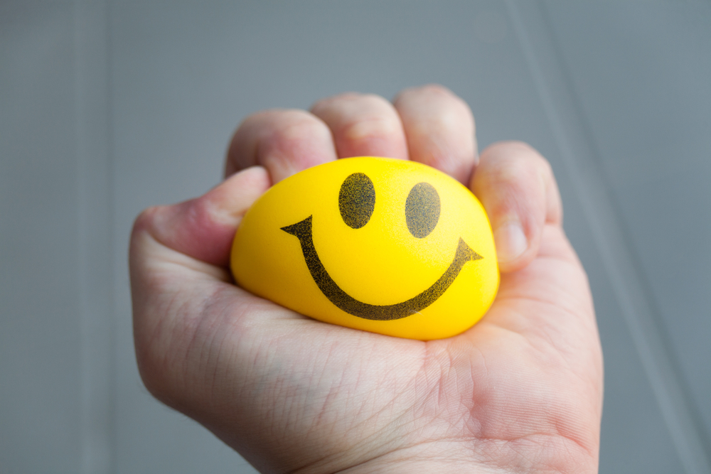 A hand squeezing their stress ball that has a smiley face on it